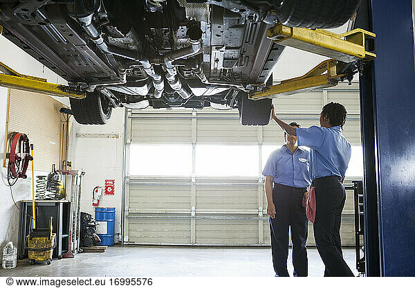 Zwei Mechanikerinnen arbeiten auf einer Hebebühne in einer Reparaturwerkstatt an der Unterseite eines Fahrzeugs