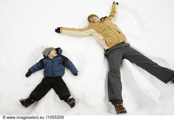 Zwei Menschen  ein Mann und ein Kind  die im Schnee liegen  bilden Schnee-Engelformen.