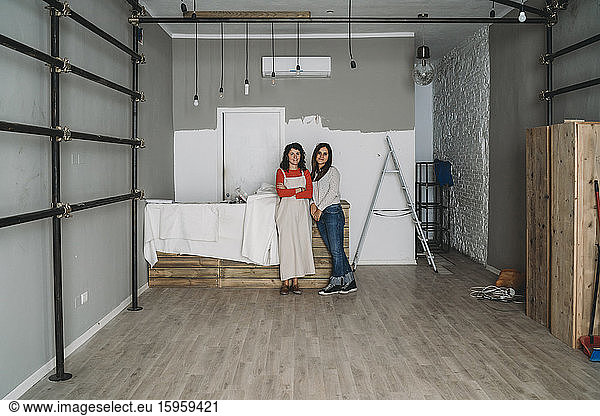 Zwei mittelgroße erwachsene Frauen  die sich in ihrem neuen Laden an einen Tisch lehnen  Porträt in voller Länge
