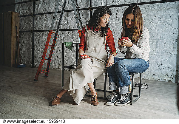 Zwei mittelgroße erwachsene Frauen schauen sich in ihrem neuen Geschäft ein Smartphone an