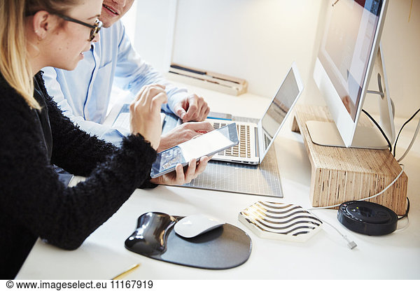 Zwei Personen an einem Arbeitsplatz  die gemeinsam an einem Tablett  einem Laptop und einem Bildschirm arbeiten.
