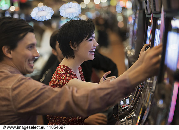 Zwei Personen  ein junger Mann und eine Frau  spielen in einem Kasino an den Spielautomaten.