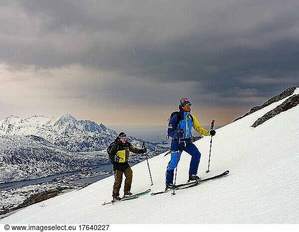 Zwei Skitourengeher im Aufstieg  bedrohliche Wolken  Insel Senja  Troms  Norwegen  Europa