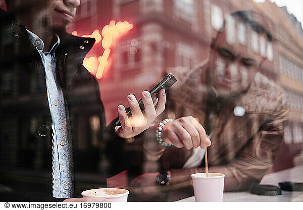 zwei unerkennbare junge hispanische Männer mit Telefon trinken Kaffee. Fokus auf das Telefon