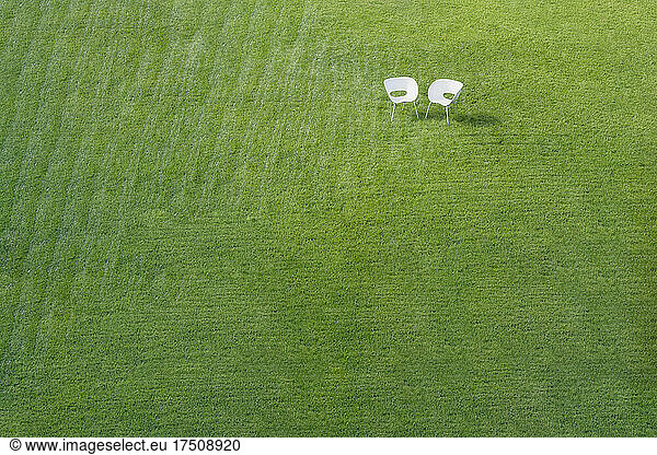 Zwei weiße Bürostühle auf grünem Rasen mit gemähtem Streifenmuster treffen sich in einer Ecke.