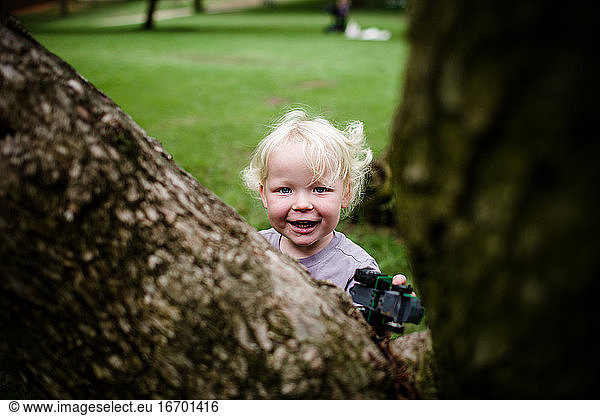 Zweijähriges Kind lächelt durch den Baum in die Kamera