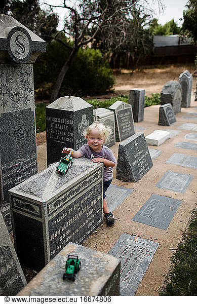 Zweijähriges Kind spielt auf Grabsteinen im Park