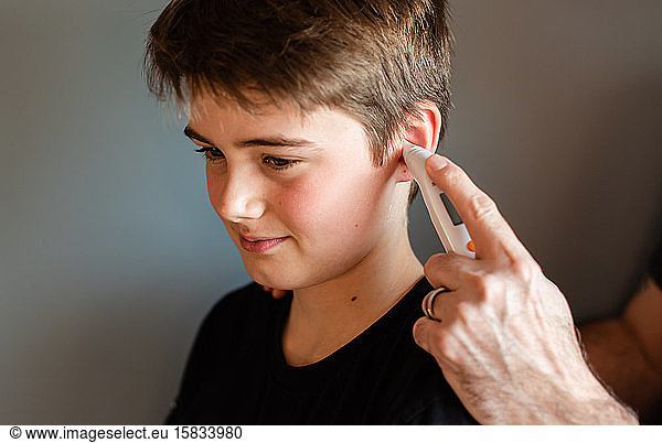 Zwischenmenschlicher Junge  der mit einem Ohrthermometer gemessen wird.
