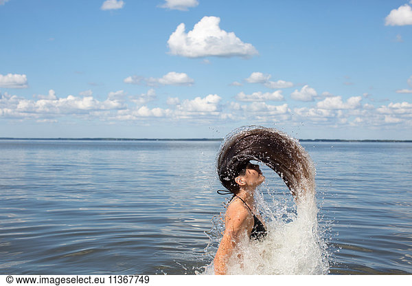 Young woman splashing and throwing back long hair from sea, Santa Rosa Beach, Florida, USA