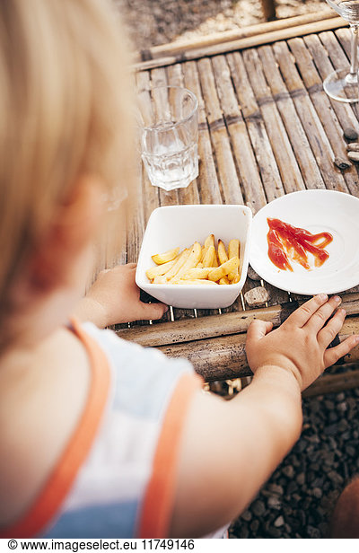 Over the shoulder view of boy eating french fries and ketchup
