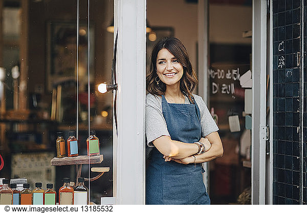 Confident female owner looking away while standing at entrance of deli